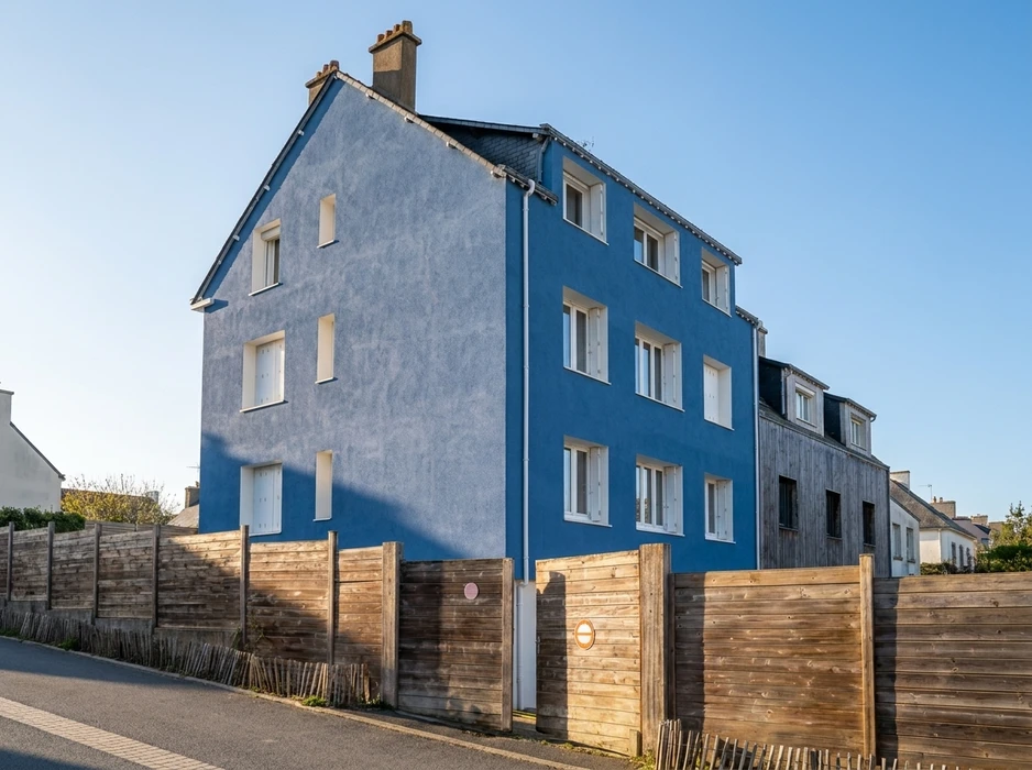 Immeuble résidentiel de trois étages, façade principale bleue vive et pignon gris clair, toiture en ardoise avec lucarnes