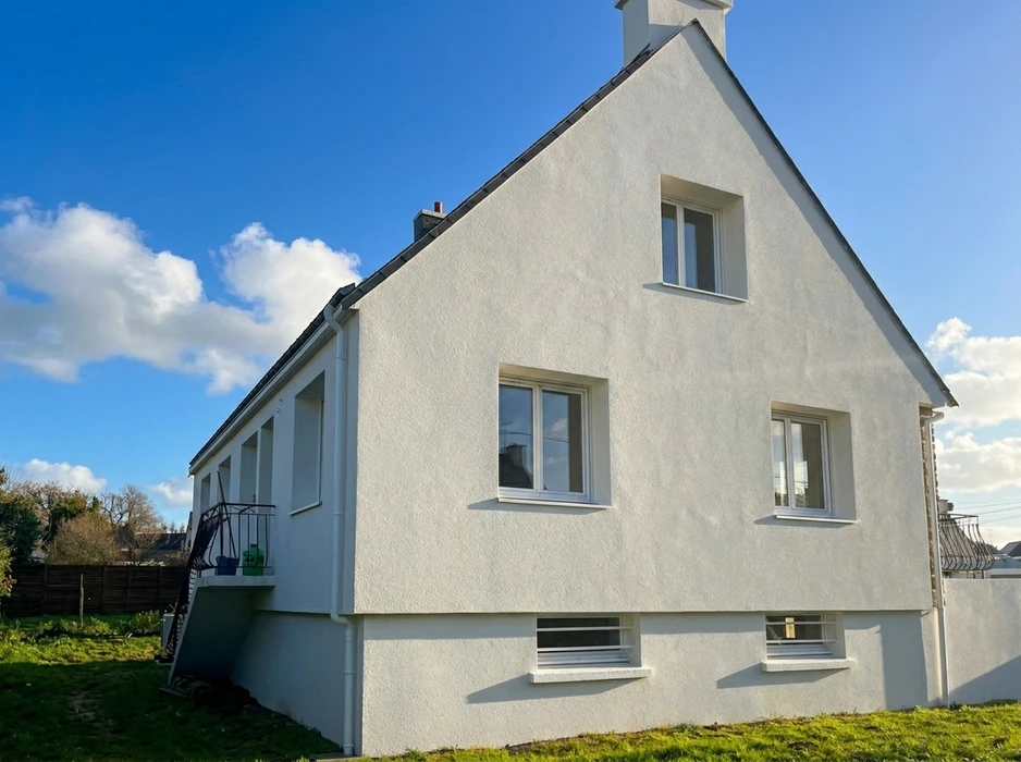 Façade latérale d'une maison individuelle rénovée, enduit de façade blanc lisse, toiture en ardoise avec cheminée