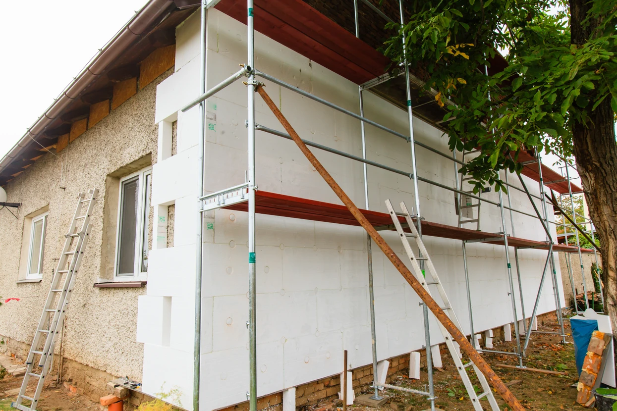 Chantier de rénovation extérieure d'une maison avec ouvriers installant un échafaudage métallique