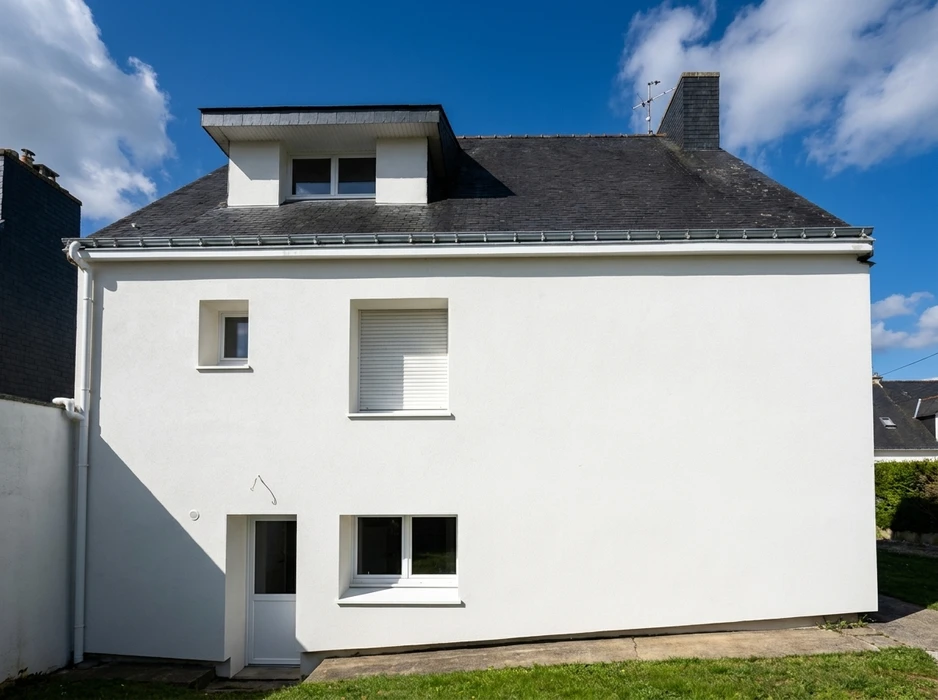 Façade arrière d'une maison individuelle blanche de style breton, toiture en ardoise naturelle avec chéneau zinc et lucarne carrée