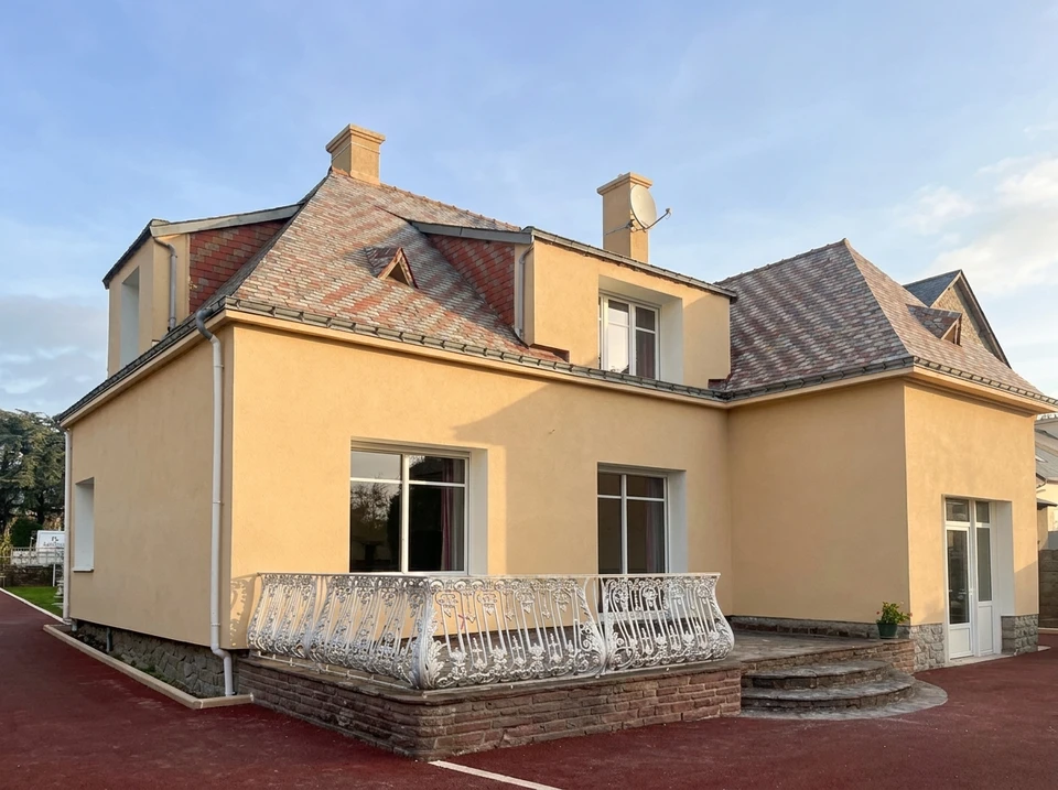 Maison individuelle moderne à deux niveaux avec façade blanche et soubassement sombre, située dans un environnement verdoyant au coucher du soleil